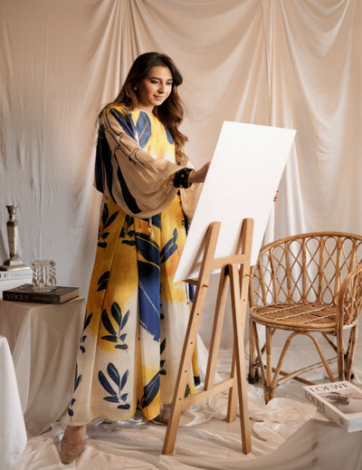 Woman in a colorful dress standing next to an easel with a blank canvas in a studio setting.